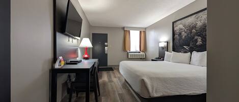 A hotel room with a bed, a desk with a chair, a TV mounted on the wall, a lamp, and an air conditioning unit.