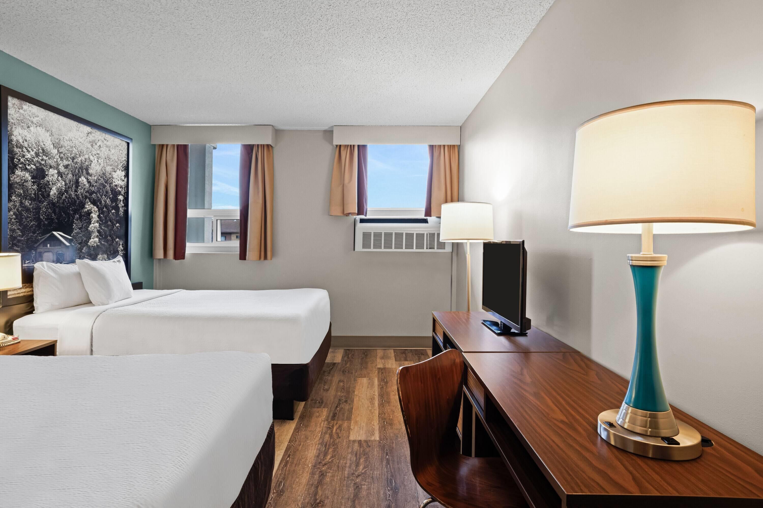 A hotel room with two beds, a desk, a chair, a lamp, a TV, and a window with curtains.