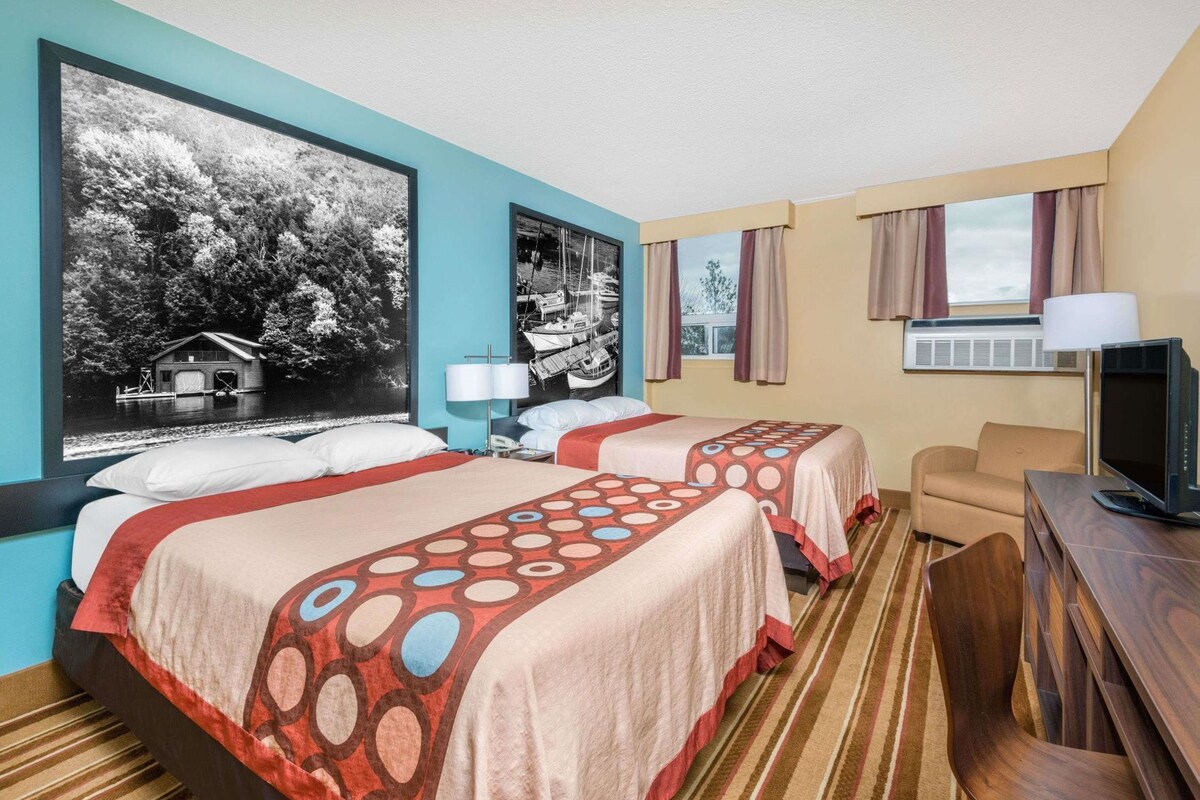 Une chambre d’hôtel avec deux lits, une télévision, un bureau et une fenêtre avec des rideaux.