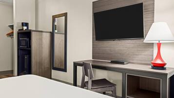 A hotel room with a bed, a desk with a chair, a TV mounted on the wall, a red lamp, and a microwave.