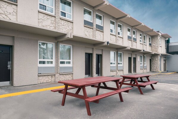 A multi-story building with a stone facade, multiple windows, and a paved parking area with red picnic tables. - Super 8 by Wyndham Thunder Bay (Thunder Bay)