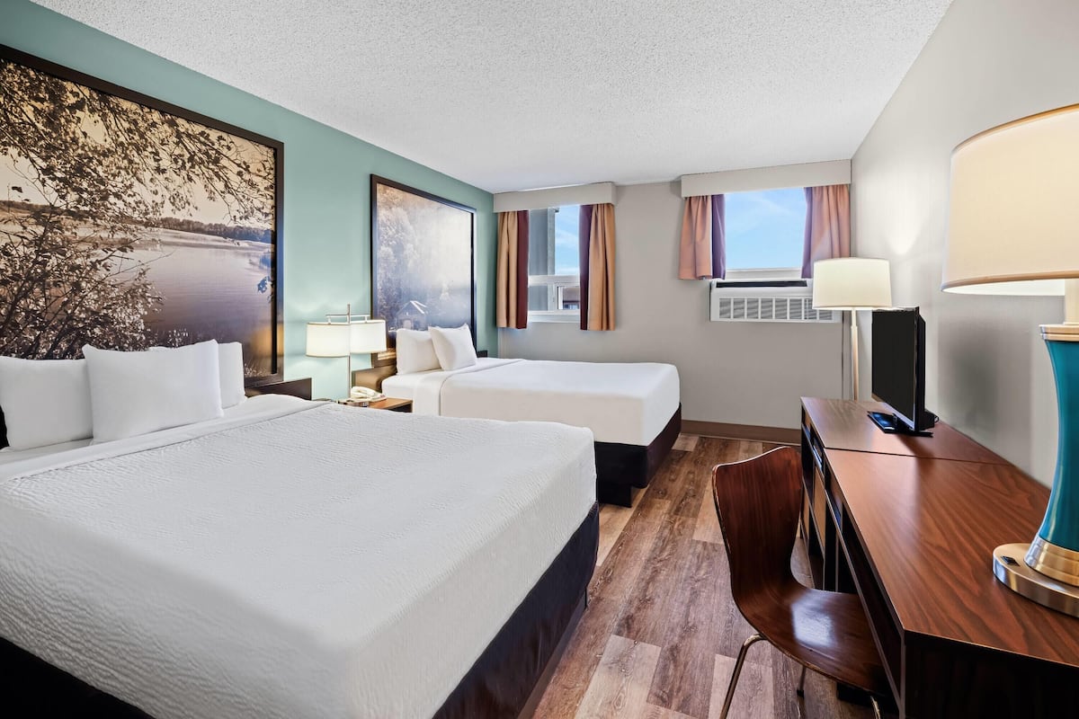Une chambre d’hôtel avec deux lits, un bureau, une chaise, une télévision et une grande fenêtre avec des rideaux.