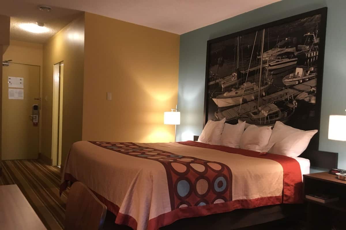 Une chambre d’hôtel avec un lit, une table de chevet, un bureau, une chaise, un tableau au mur et une porte.