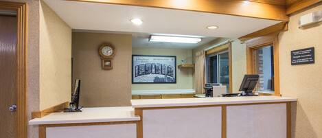 A reception desk with a clock, a framed welcome sign, and a window with blinds.
