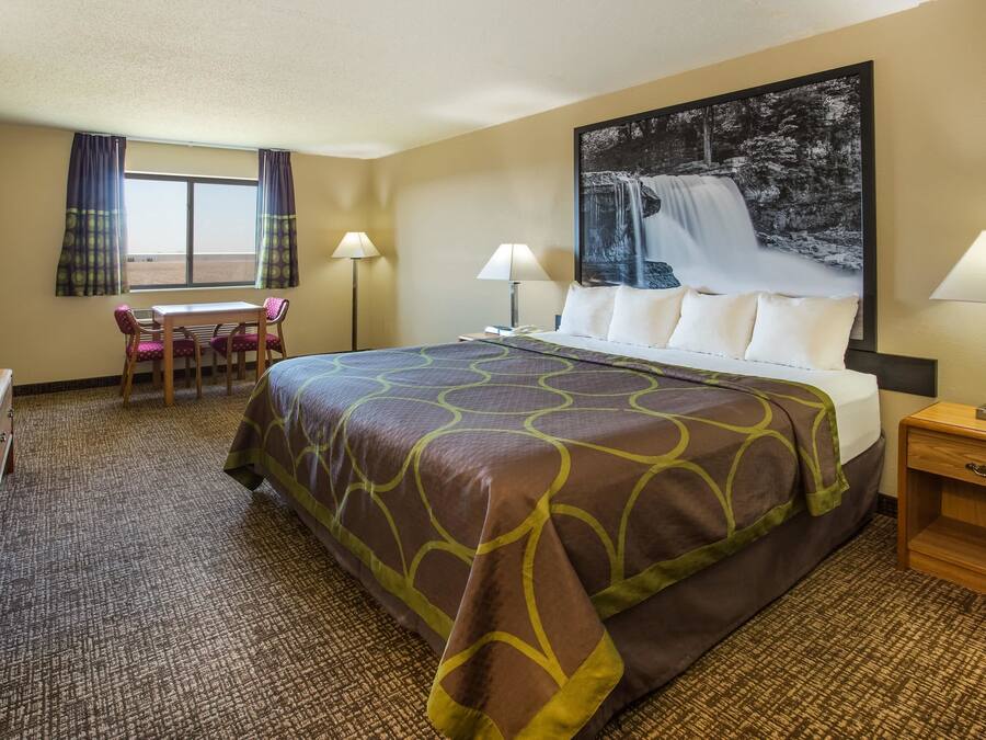 A hotel room with a large bed, two bedside lamps, a desk with a chair, a TV, and a window with curtains.