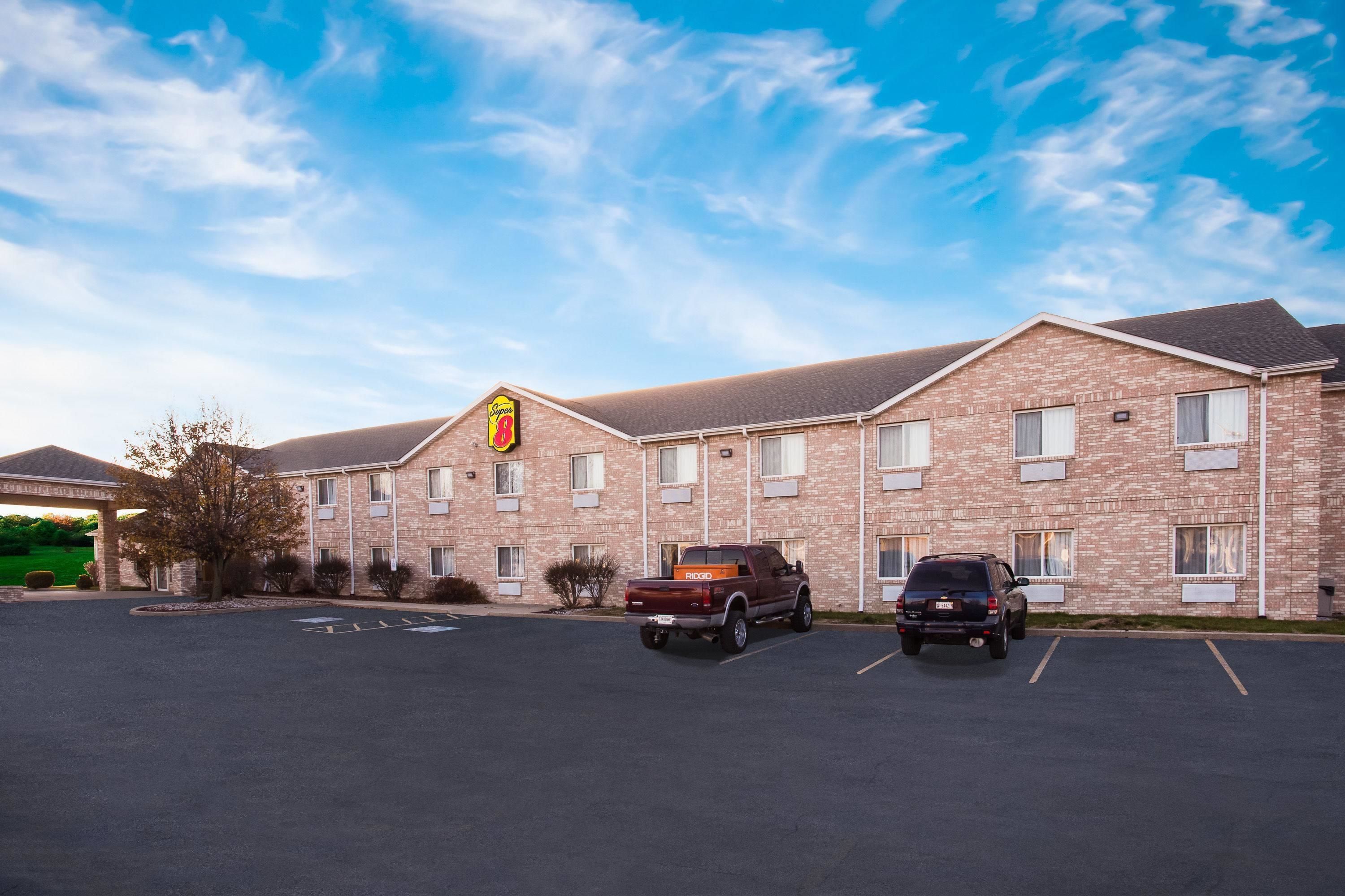A hotel with a brick facade, multiple windows, and a parking lot with two cars.