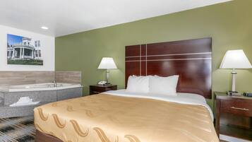 Habitación de hotel con una cama grande, dos mesitas de noche con lámparas, una bañera integrada y un cuadro colgado en la pared.