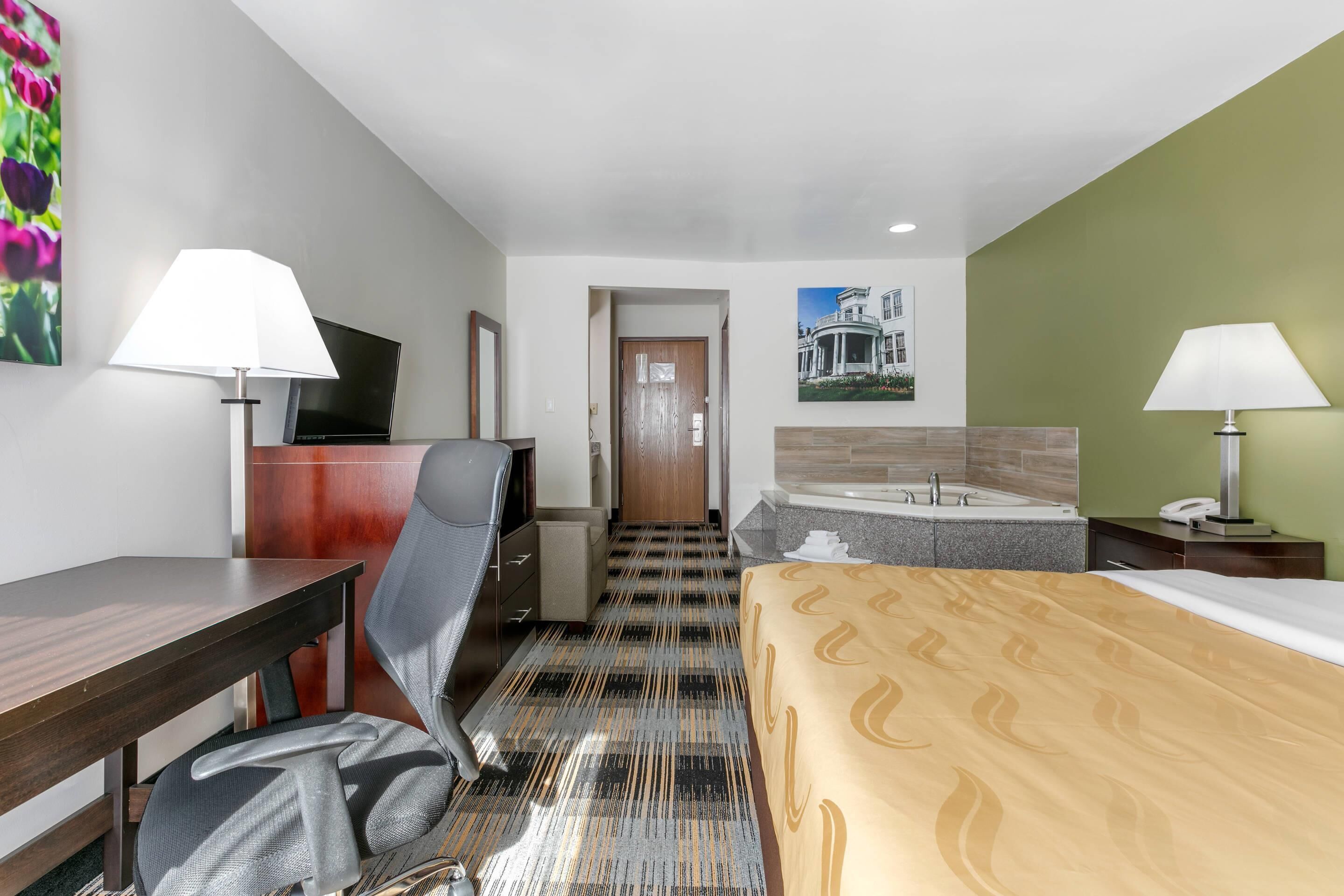 Una habitación de hotel con cama, escritorio, silla, televisor y baño con bañera.