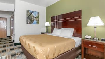 A hotel room with a large bed, two bedside lamps, a wooden headboard, a painting on the wall, and a door leading to another room.