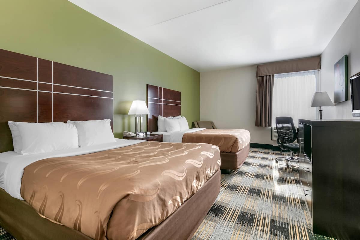 Habitación de hotel con dos camas, un escritorio, una silla, un televisor y una ventana con cortinas.