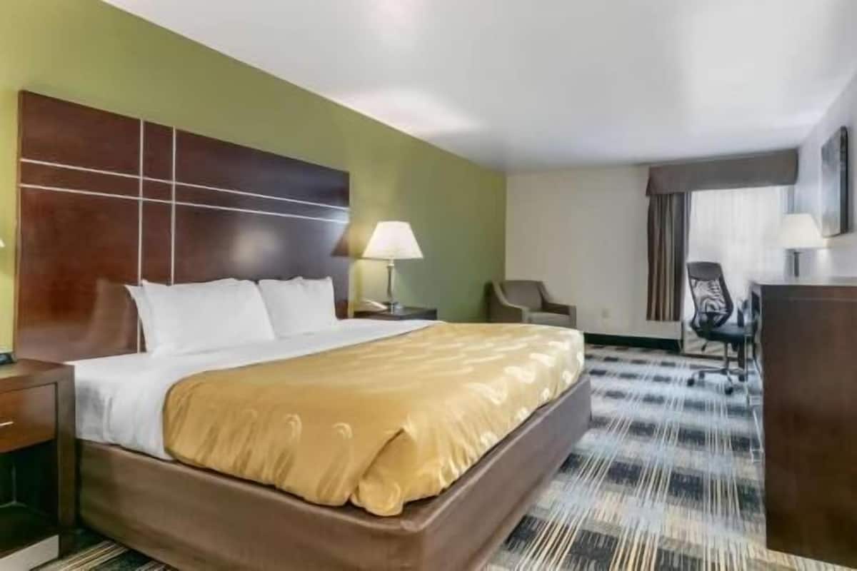 Una habitación de hotel con cama, mesita de noche, silla, escritorio y lámpara.