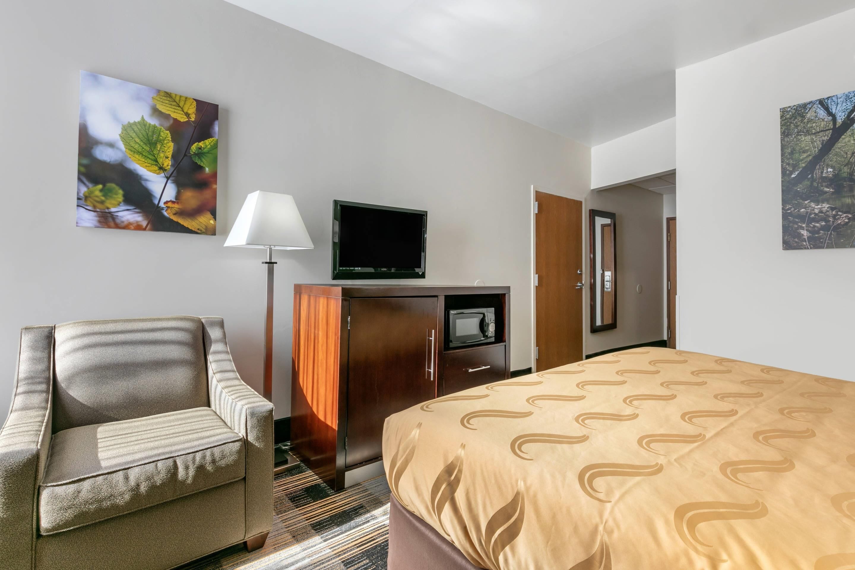 A hotel room with a bed, a chair, a television, a wardrobe, and a desk.