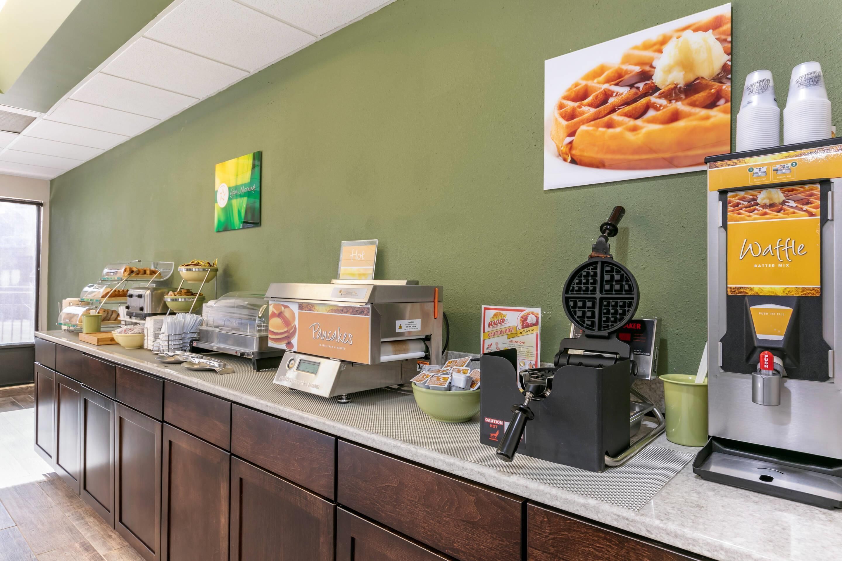 Un bar à petit-déjeuner équipé de machines à gaufres et à crêpes, d’un présentoir à gaufres et d’un panneau indiquant les boissons chaudes.
