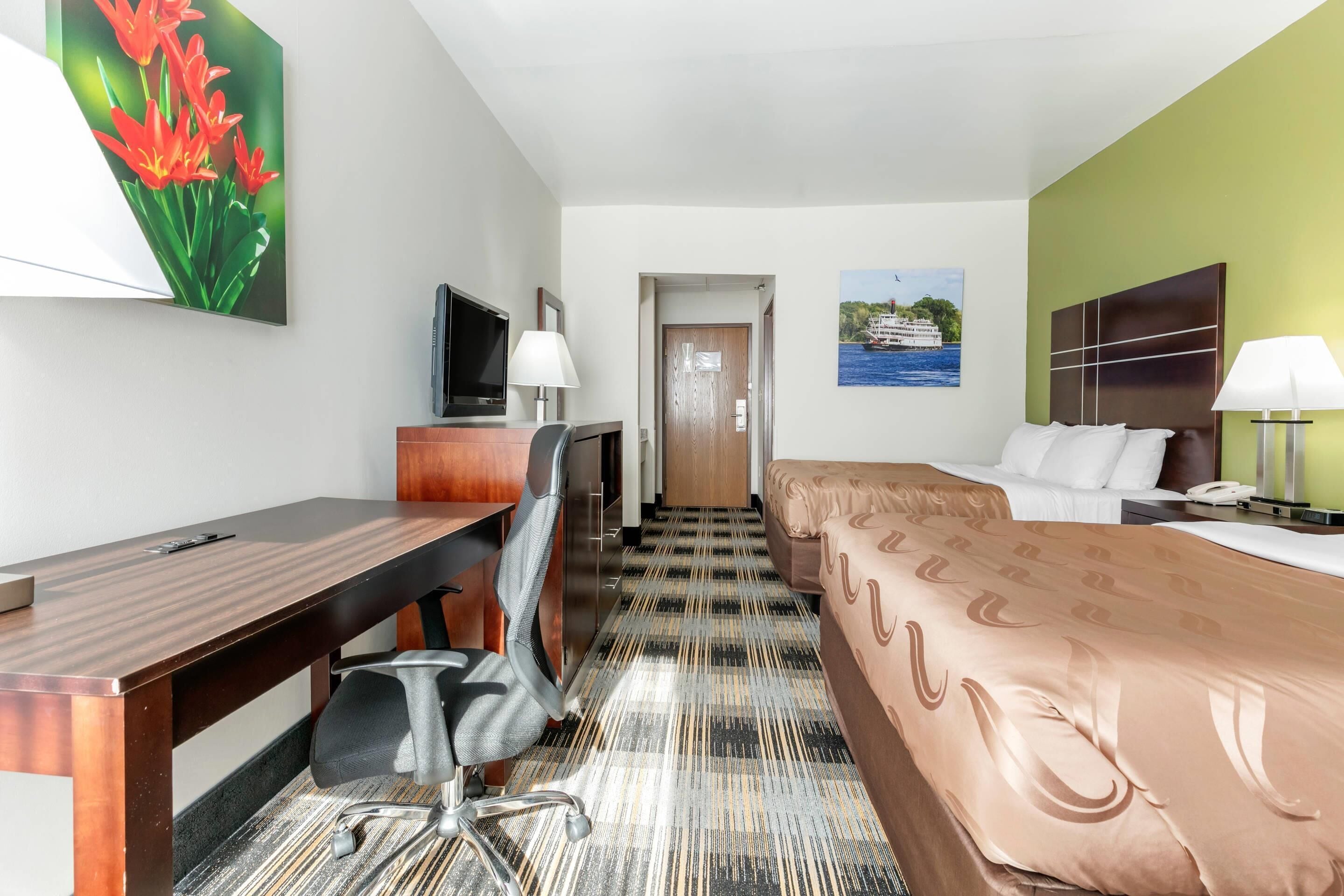 A hotel room with a bed, desk, chair, TV, and a painting on the wall.