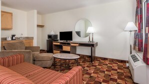 A hotel room with a sofa, a round coffee table, a TV, a desk with a computer, a mirror, and an air conditioner. - Super 8 by Wyndham Fayetteville (Fayetteville)