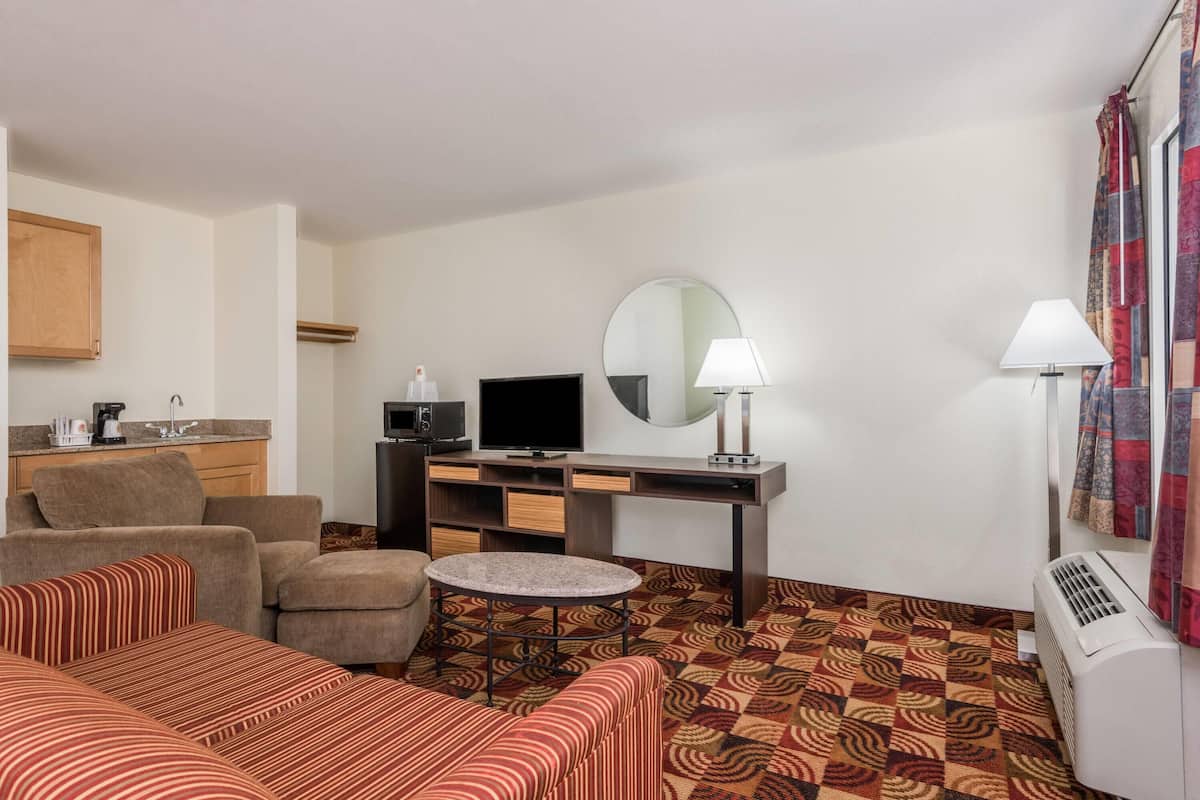 Habitación de hotel con sofá, una mesita redonda, televisión, escritorio con computadora, espejo y aire acondicionado.