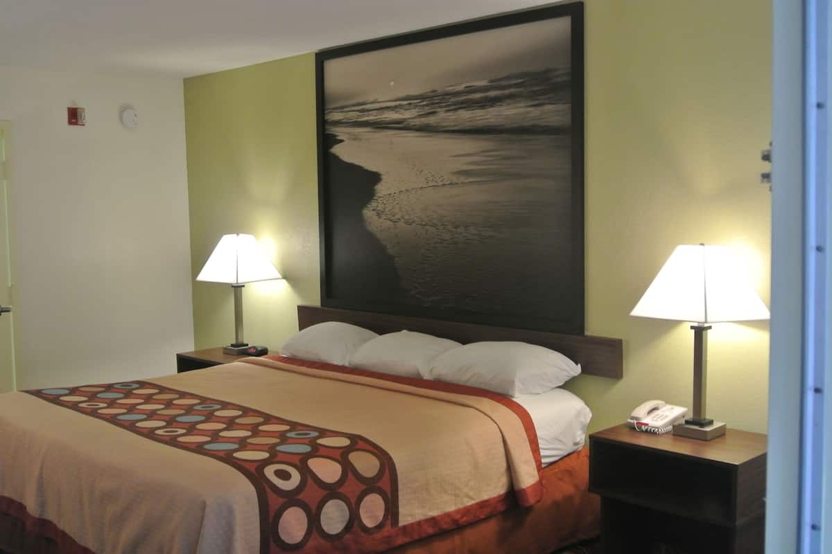 Habitación de hotel con cama, dos lámparas de noche, mesita de noche con teléfono y un cuadro grande en la pared.