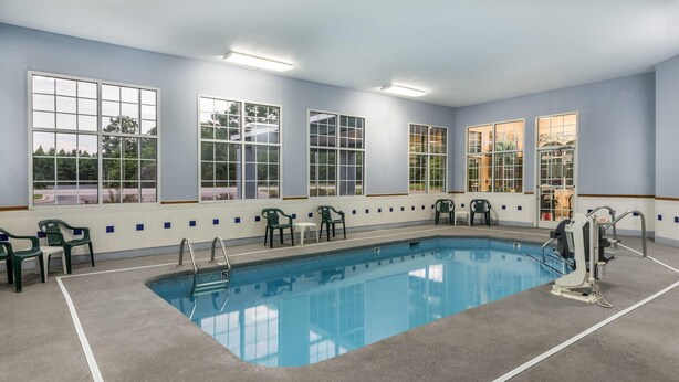 A swimming pool with clear blue water, surrounded by green chairs and a lifeguard chair, with large windows offering views of the outside. - Super 8 by Wyndham Fayetteville (Fayetteville)