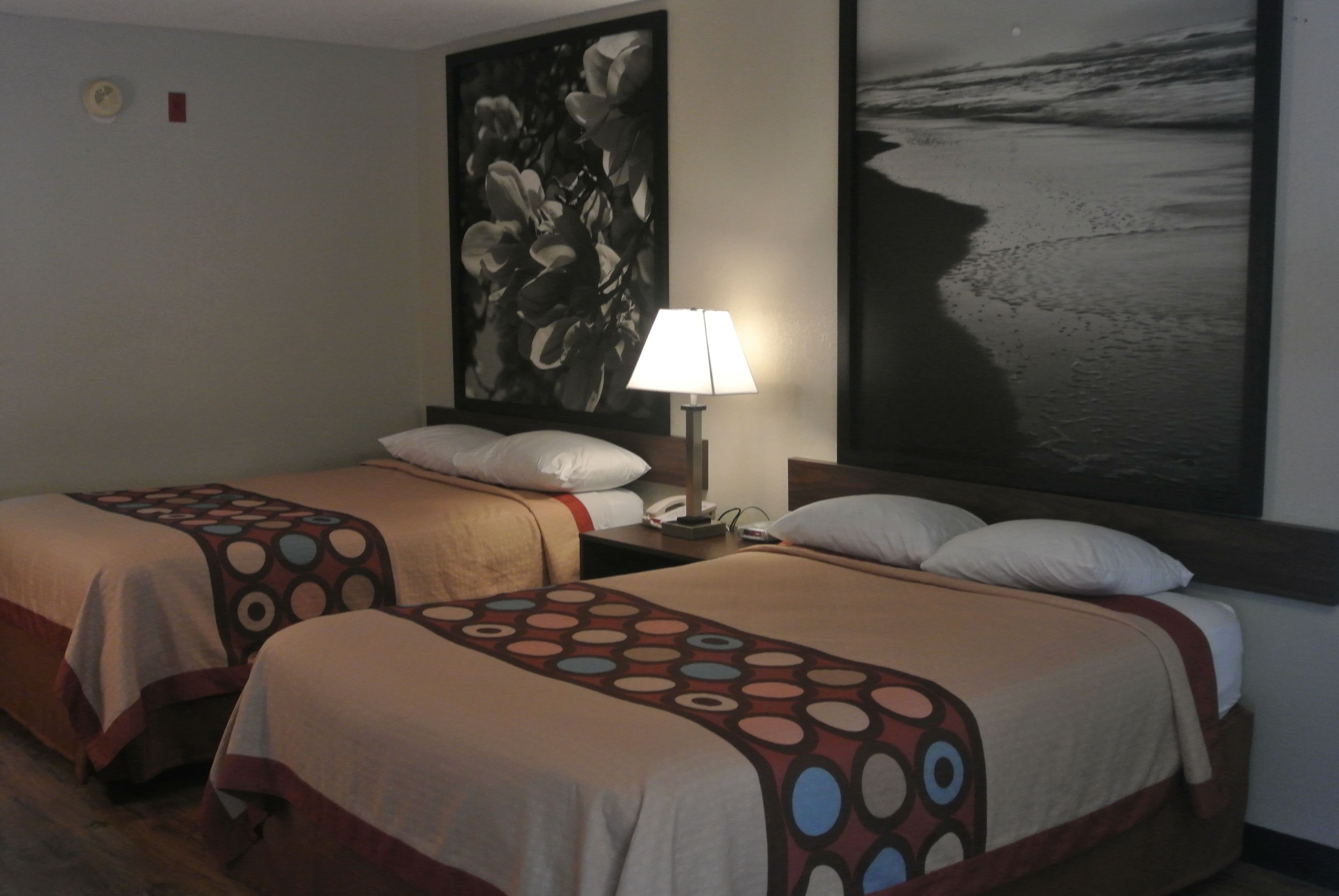 Une chambre d’hôtel avec deux lits, chacun recouvert d’une couvre-lit à motifs, une table de chevet avec une lampe et un grand tableau abstrait accroché au mur.