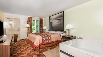 A hotel room with a bed, a desk, a chair, a large window with curtains, a painting on the wall, and a bathtub.