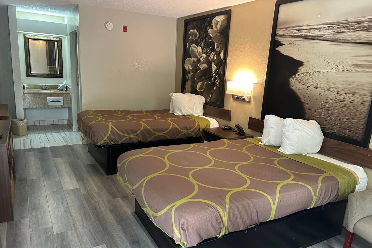 Habitación de hotel con dos camas, baño con espejo y un cuadro grande con temática playera en la pared.