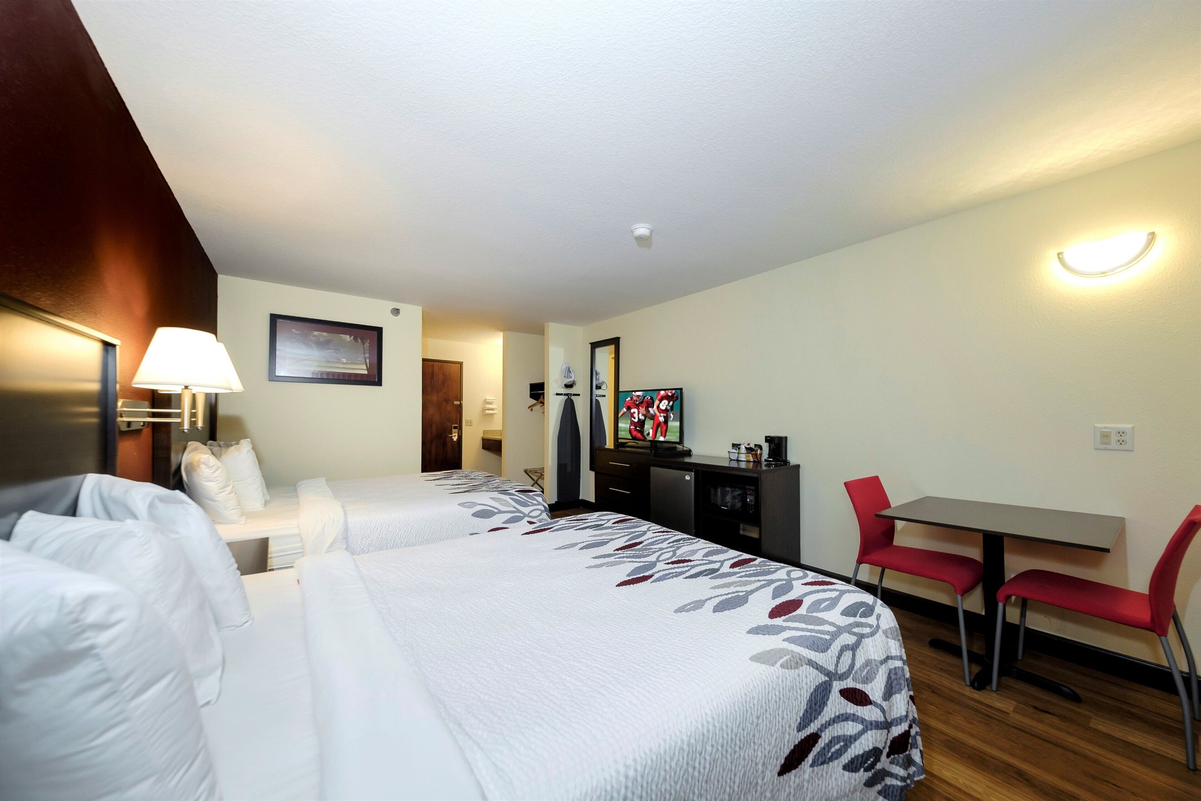 Habitación de hotel con dos camas, un escritorio, una silla, un televisor y una lámpara fijada a la pared.