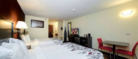 Quarto de hotel com duas camas, uma escrivaninha, uma cadeira, uma televisão e luminária na parede.