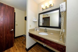 Un baño con puerta de madera, un lavamanos con espejo y un secador de pelo en la pared.