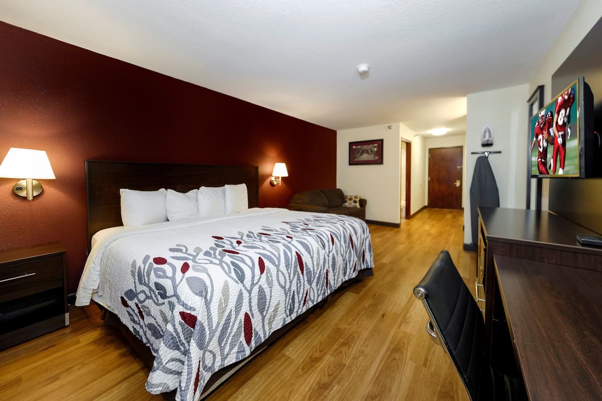 A hotel room with a large bed, two bedside lamps, a wooden dresser, a television, and a framed picture on the wall.