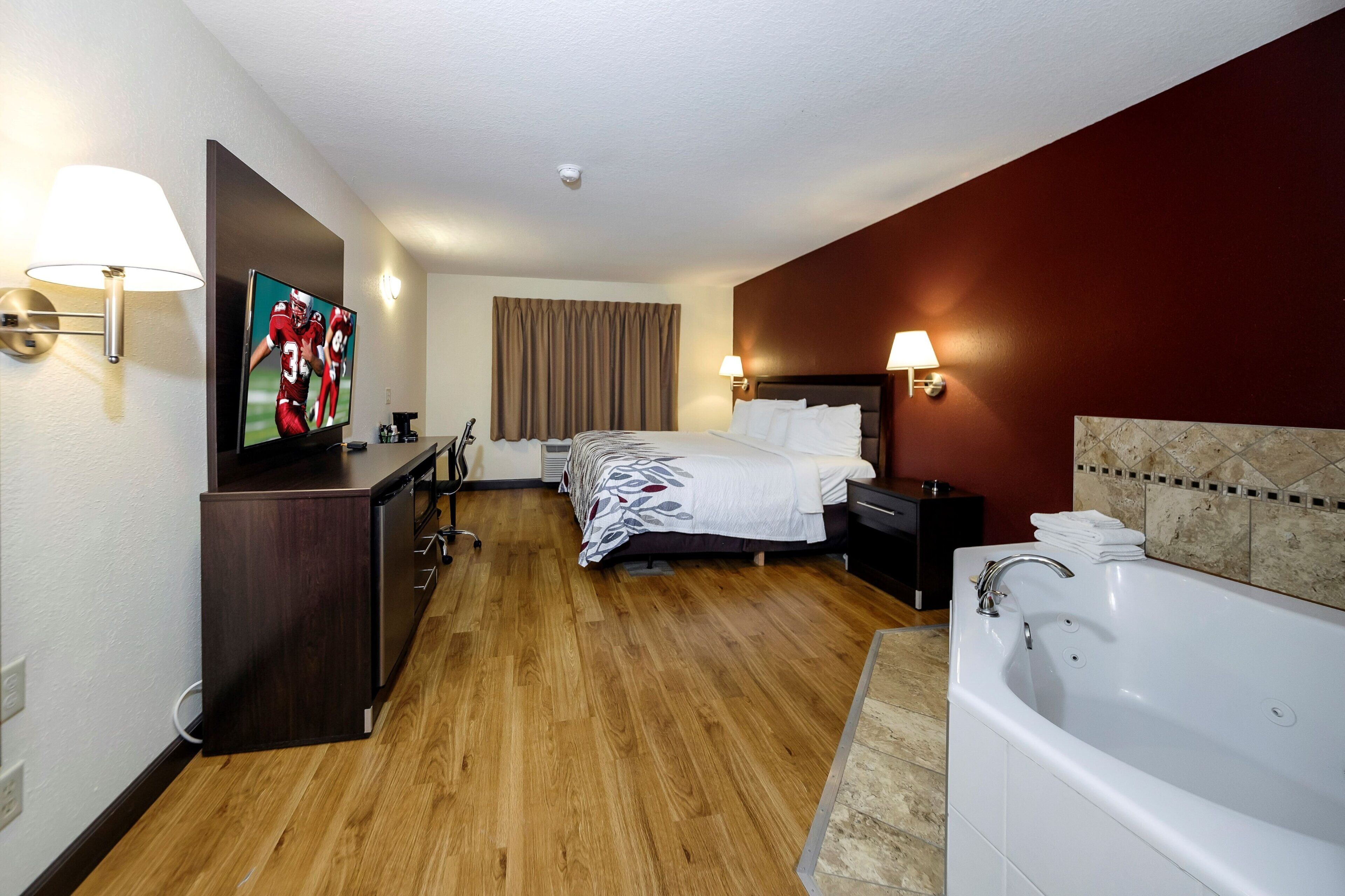 Habitación de hotel con cama, escritorio, televisor y baño privado con bañera y ducha.