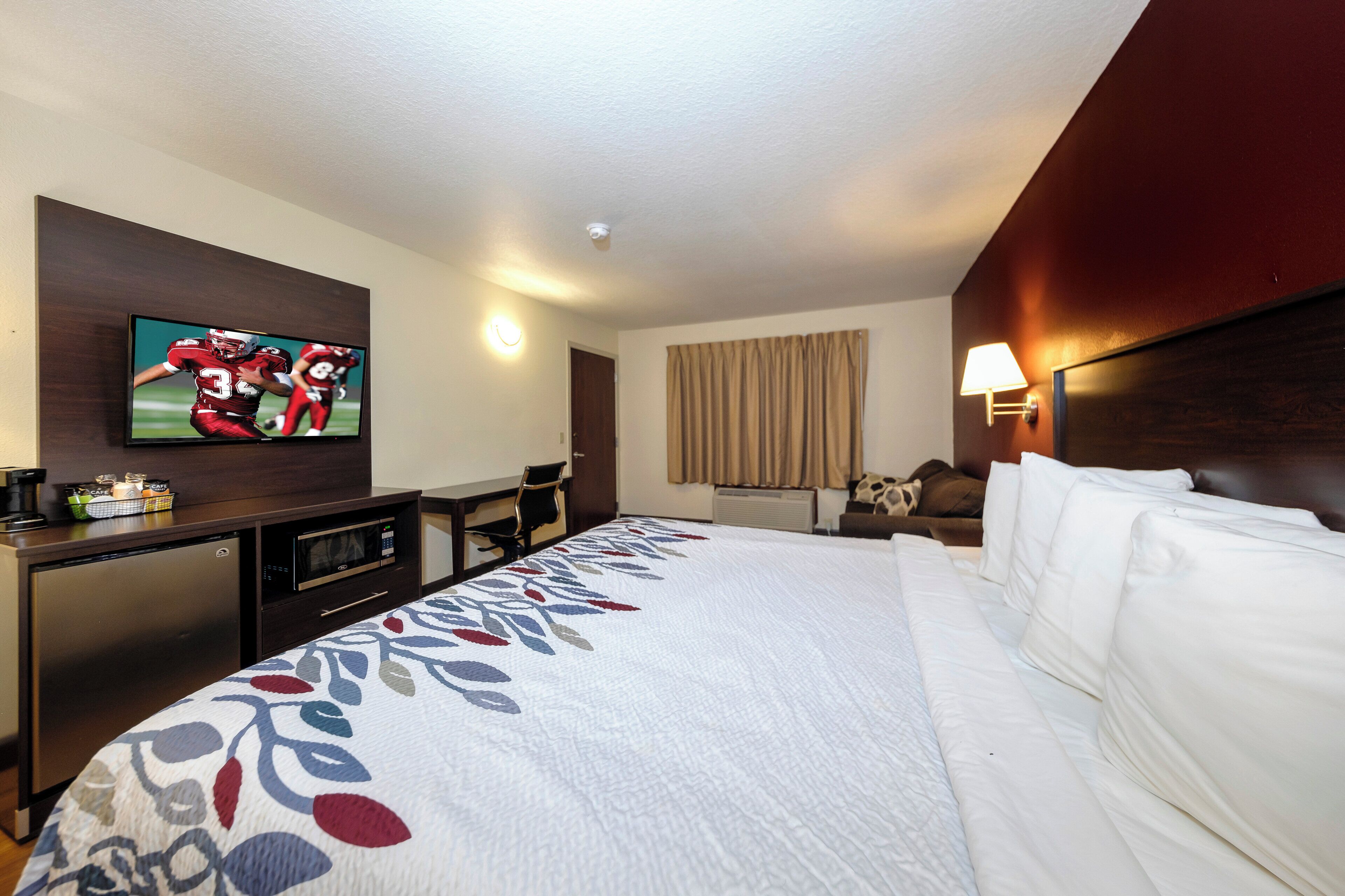 Habitación de hotel con cama, televisión montada en la pared, escritorio con microondas y una silla.
