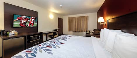 Habitación de hotel con cama, televisión montada en la pared, escritorio con microondas y una silla.