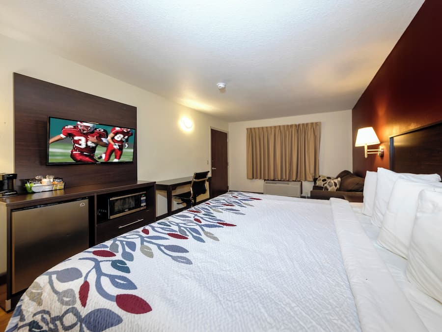 A hotel room with a bed, a television mounted on the wall, a desk with a microwave, and a chair.