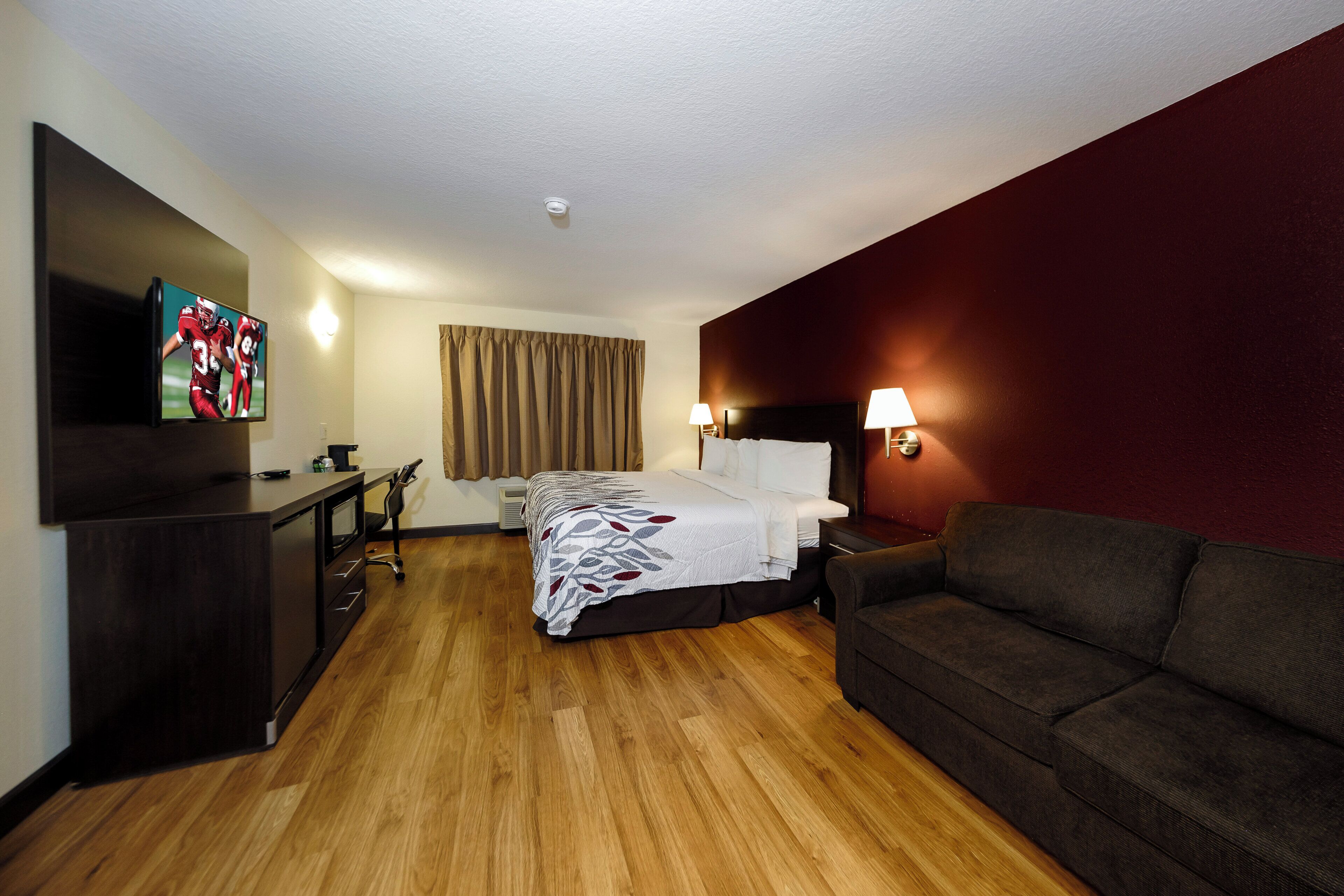 Una habitación de hotel con una cama, un escritorio, un televisor, un sofá y una lámpara de pared.