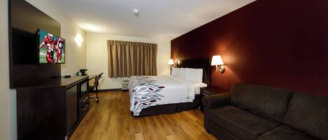 A hotel room with a bed, a desk, a television, a couch, and a wall-mounted lamp.