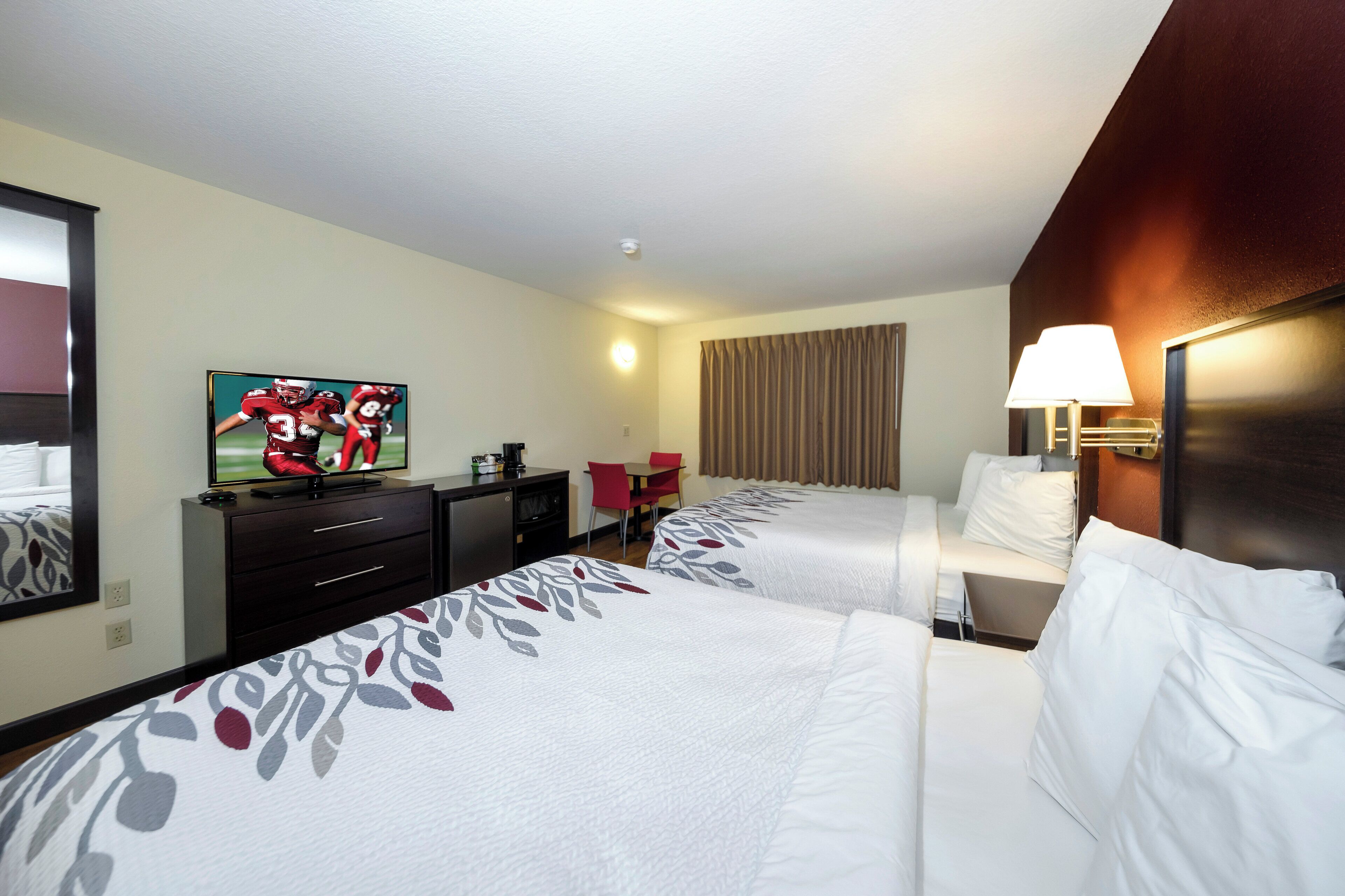 A hotel room with two beds, a TV, a desk, a chair, a lamp, and a window with curtains.
