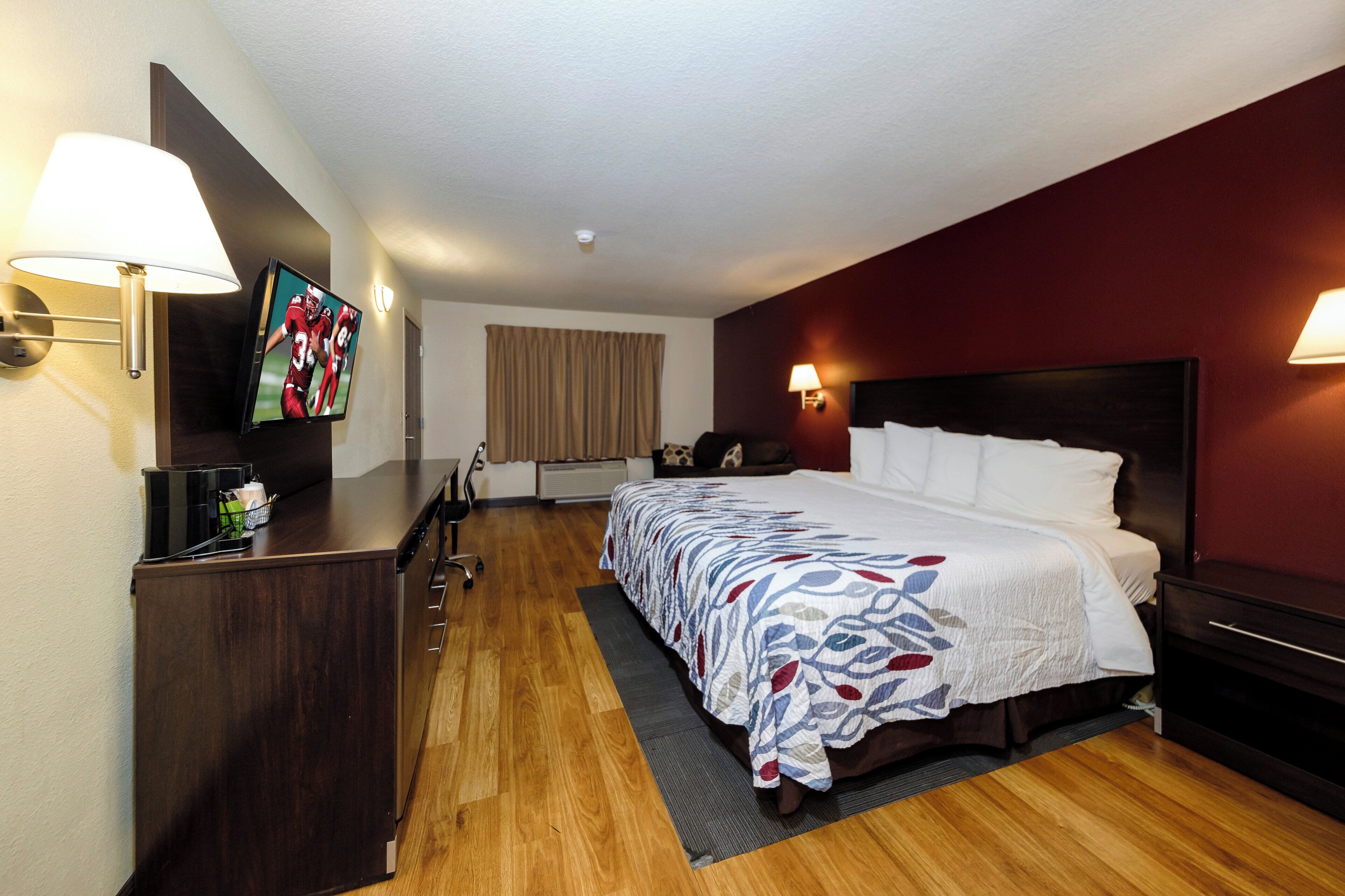 Habitación de hotel con cama, escritorio, televisor y ventana con cortinas.