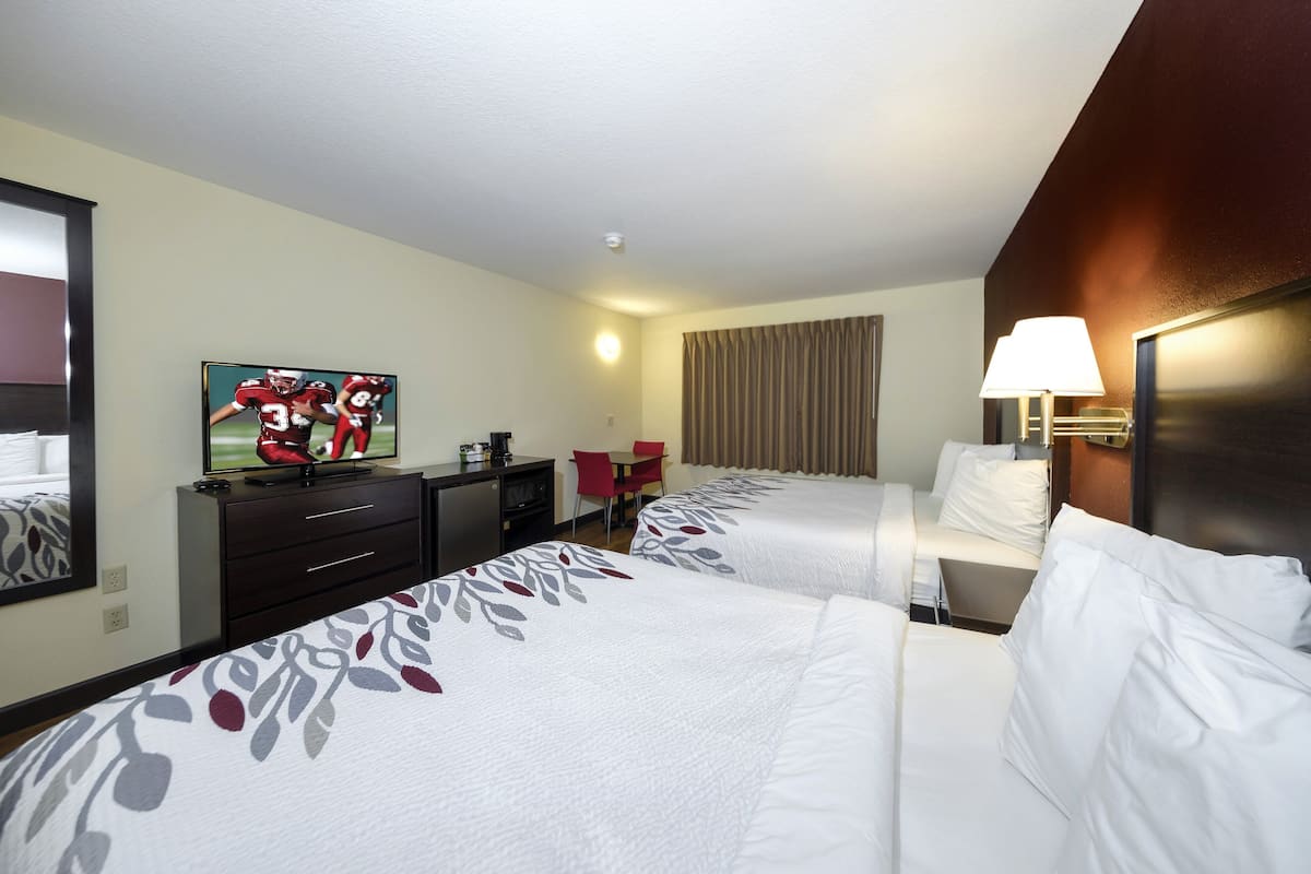 A hotel room with two beds, a TV, a desk, a chair, and a lamp.