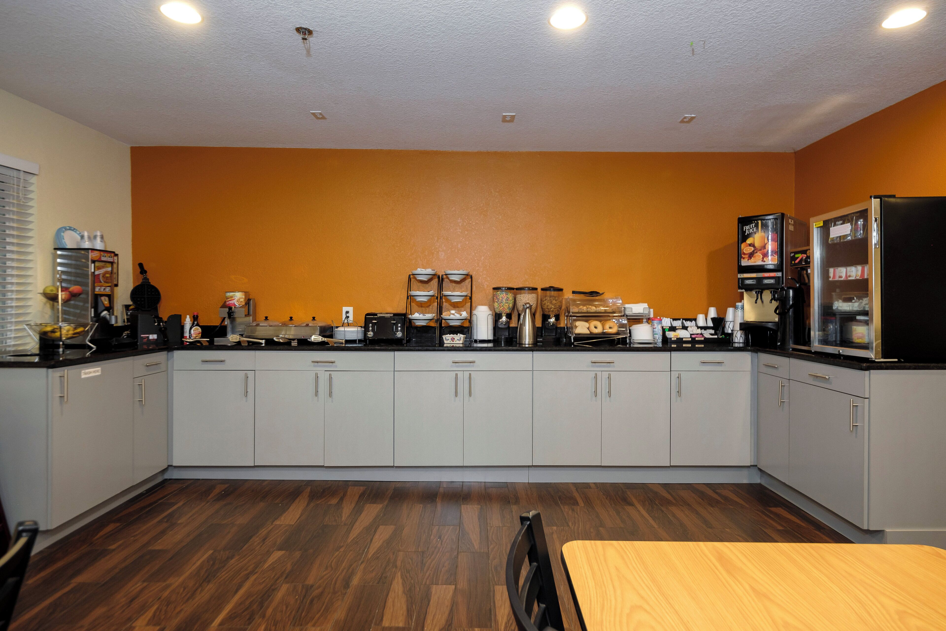 Una cocina con armarios grises, una mesa de madera y un dispensador de jugo de frutas.