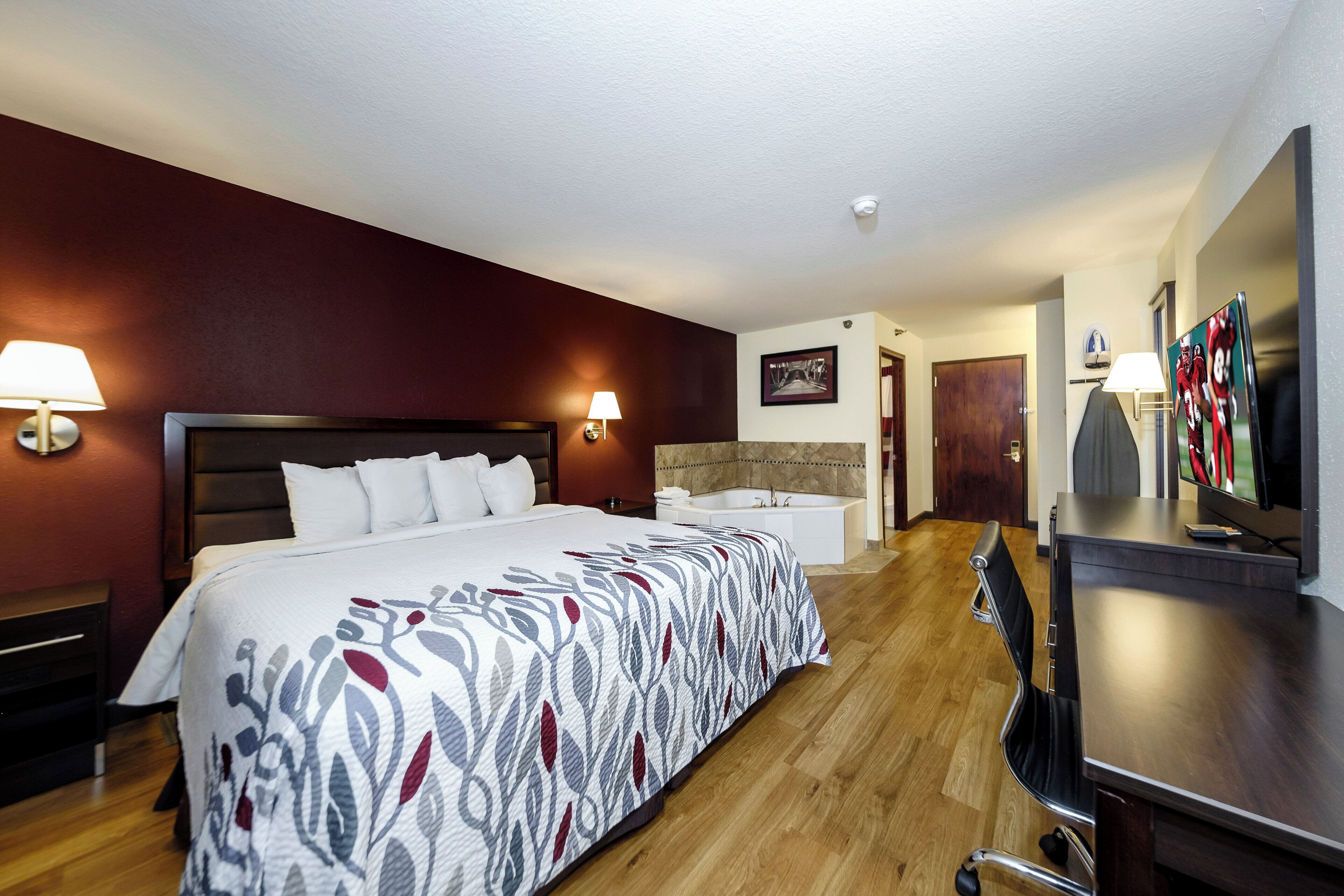 A hotel room with a large bed, a desk, a television, and a bathroom.