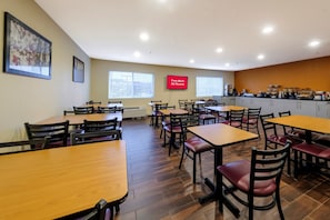 Un área de comedor con varias mesas y sillas, un televisor mostrando 'Wi-Fi gratuito en todas las habitaciones' y una cocina con alimentos.