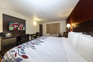 Habitación de hotel con cama, televisor montado en la pared, escritorio con microondas y un refrigerador pequeño.