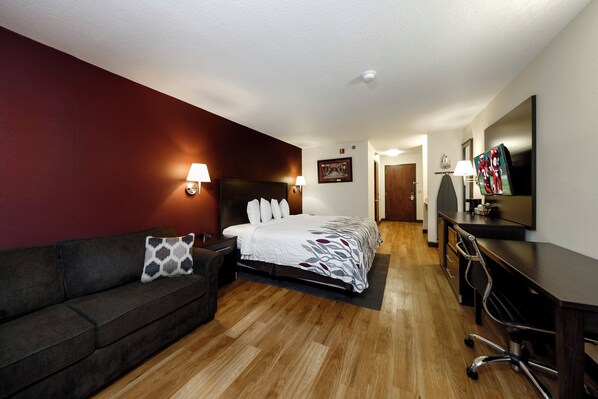 A hotel room with a bed, a desk, a chair, a sofa, and a television.