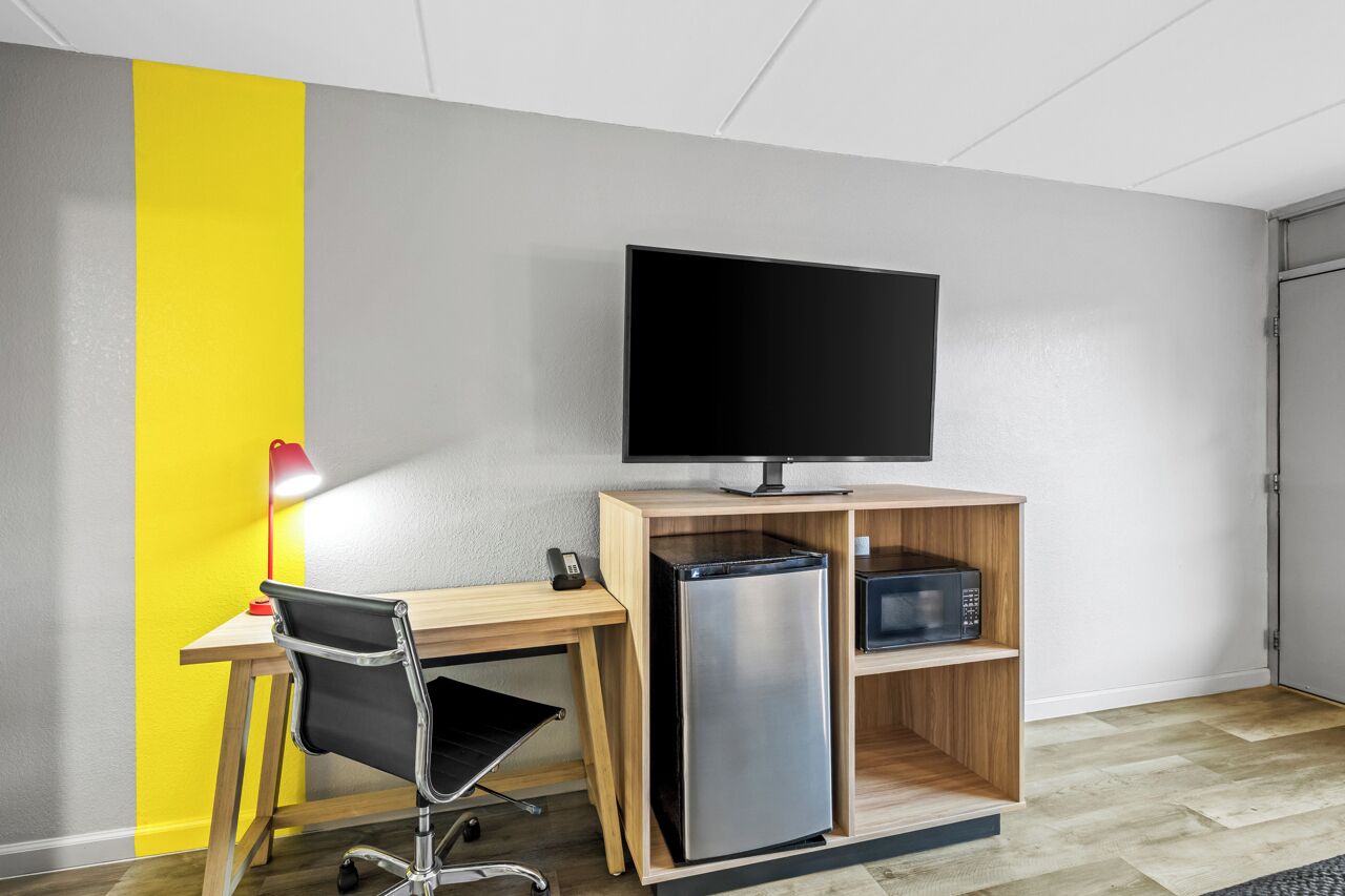 A modern room with a wooden desk, a black office chair, a flat-screen TV, a refrigerator, and a microwave.