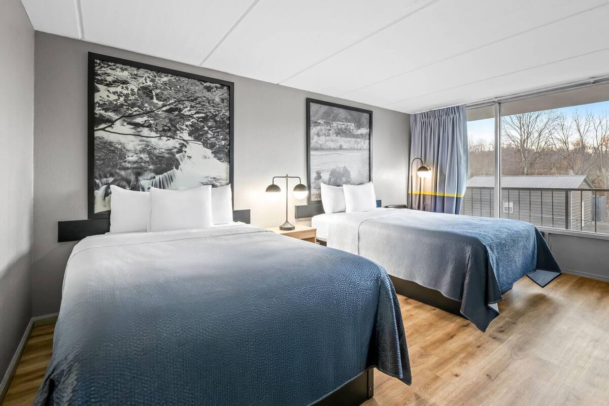 Habitación de hotel con dos camas, un ventanal grande y dos lámparas fijadas a la pared.