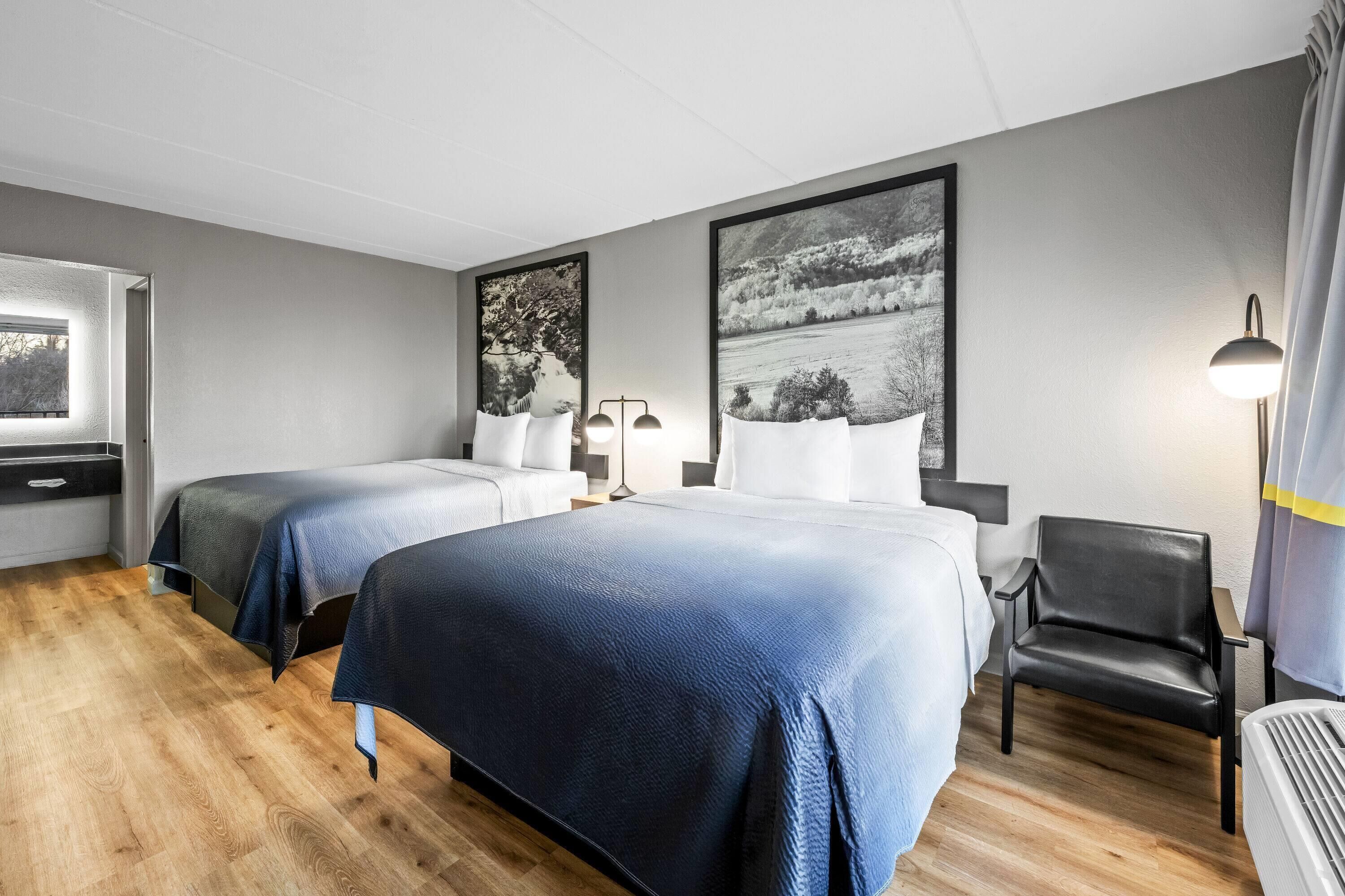 Una habitación de hotel con dos camas, una silla, un escritorio y una ventana.