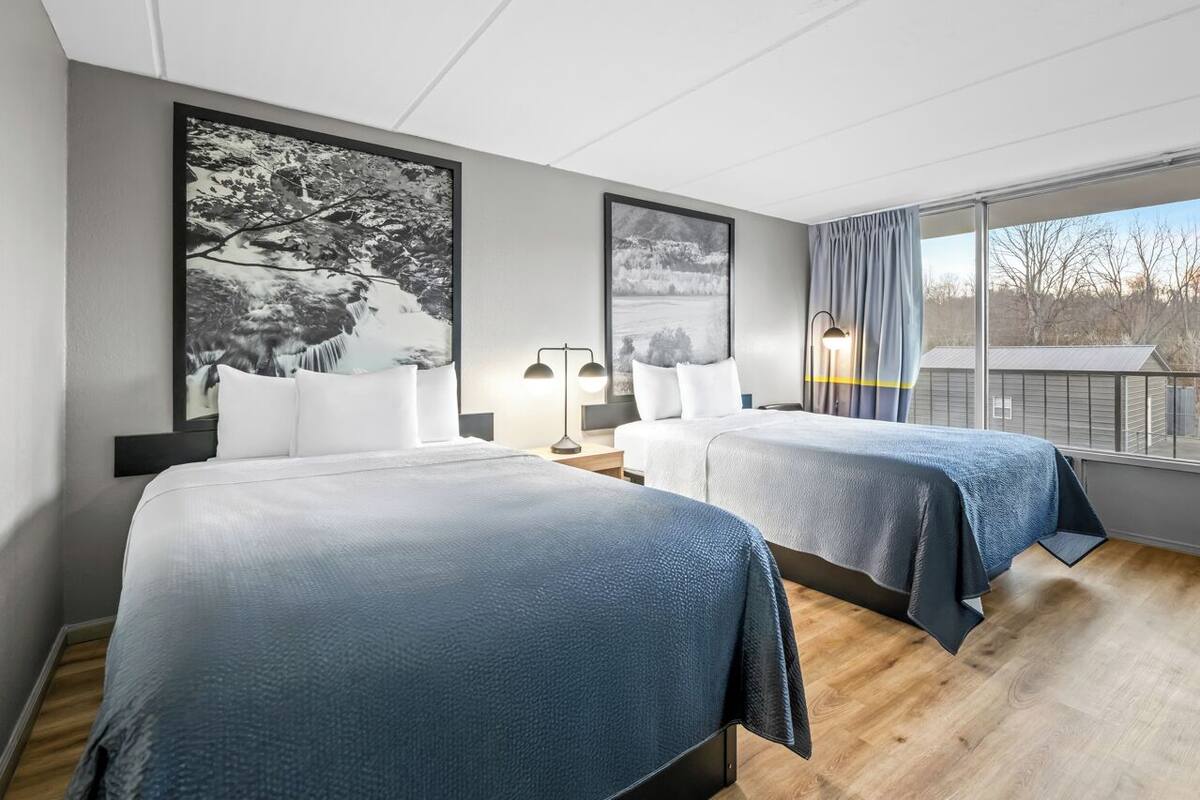 Habitación de hotel con dos camas, un ventanal con vistas y obras de arte en las paredes.