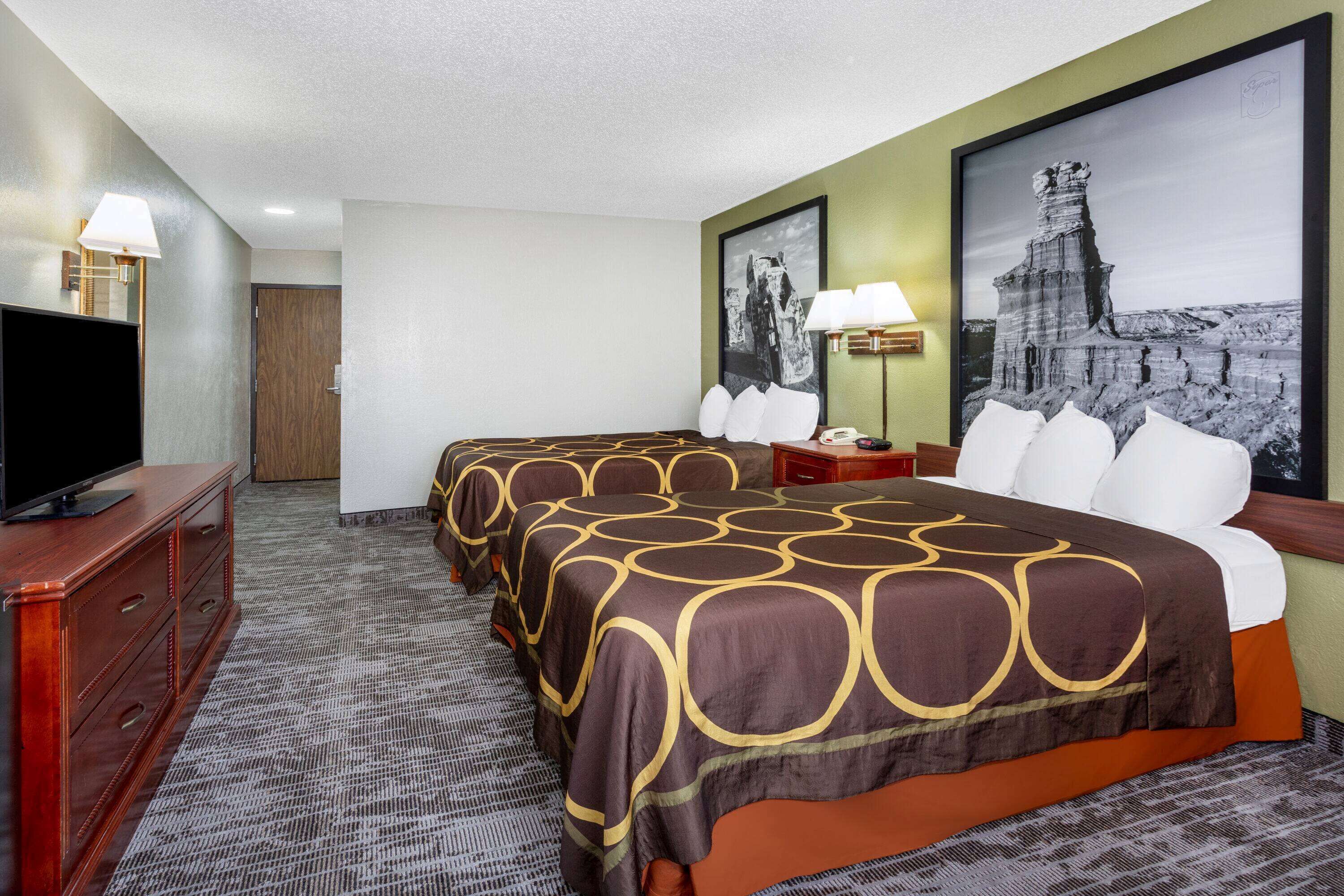 Una habitación de hotel con dos camas, televisión, escritorio y lámpara.