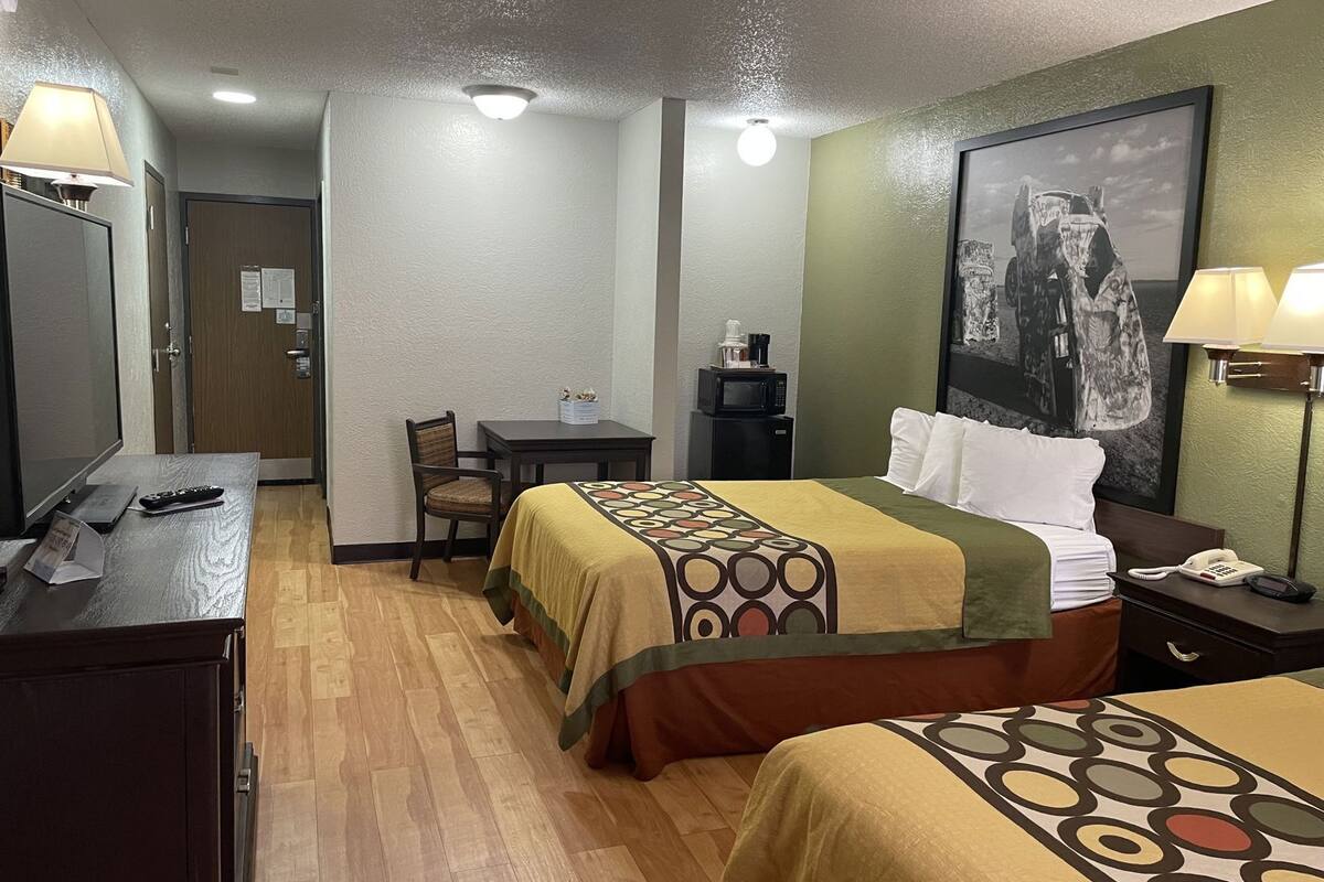 A hotel room with two beds, a desk, a chair, a microwave, a telephone, and a framed picture on the wall.