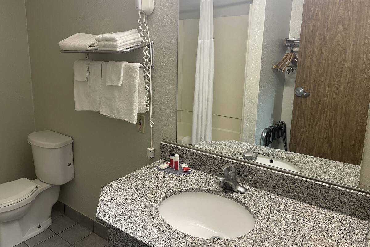 A bathroom with a granite sink, a white toilet, a towel rack with folded towels, a hairdryer, and a shower curtain.